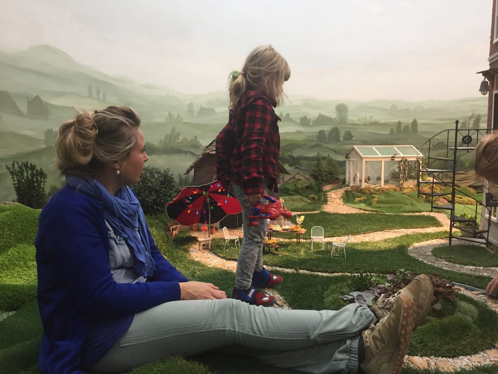 A mother and a small child sit in the studio's miniature garden, among the tiny chairs and a parasol