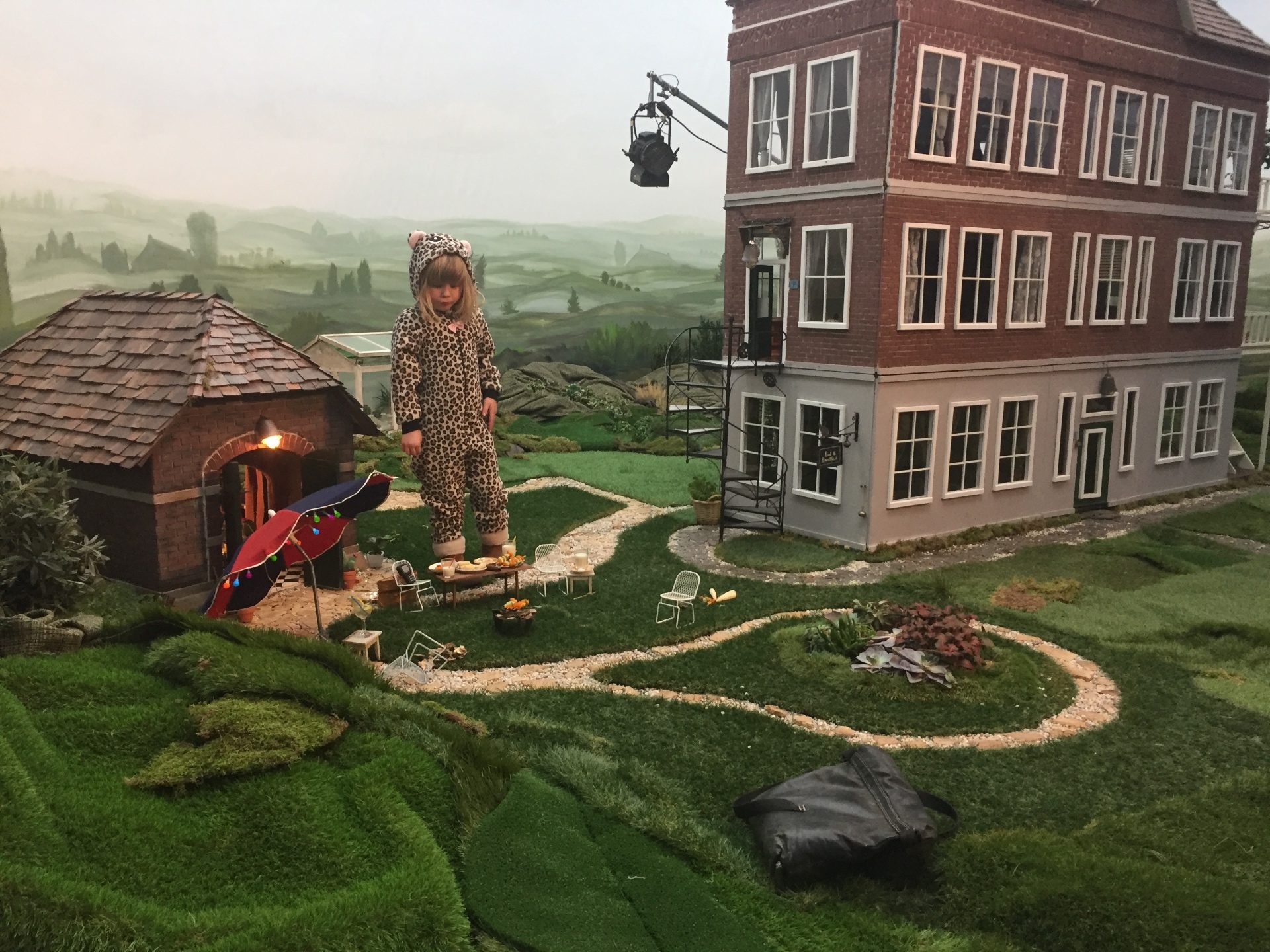 A child in a leopard suit stands in the middle of the miniature village, with the painted hills in the background